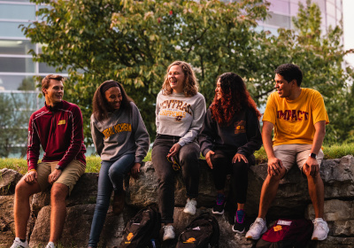 Five Central Michigan University students are seated on outside near the Charles V. Park Library wearing Central Michigan University clothing.