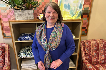 A woman wearing a blue shirt and paisley scarf is smiling.