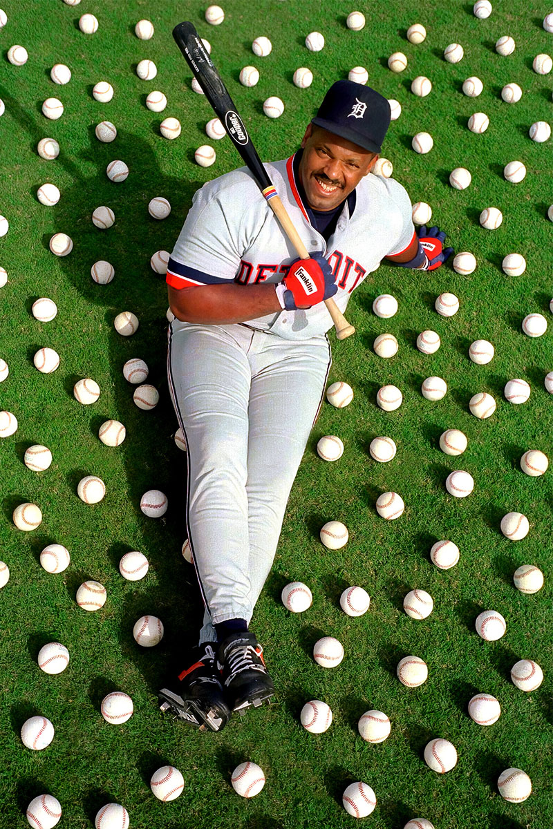 A baseball playing holding a bat while sitting on the ground with baseballs around him.