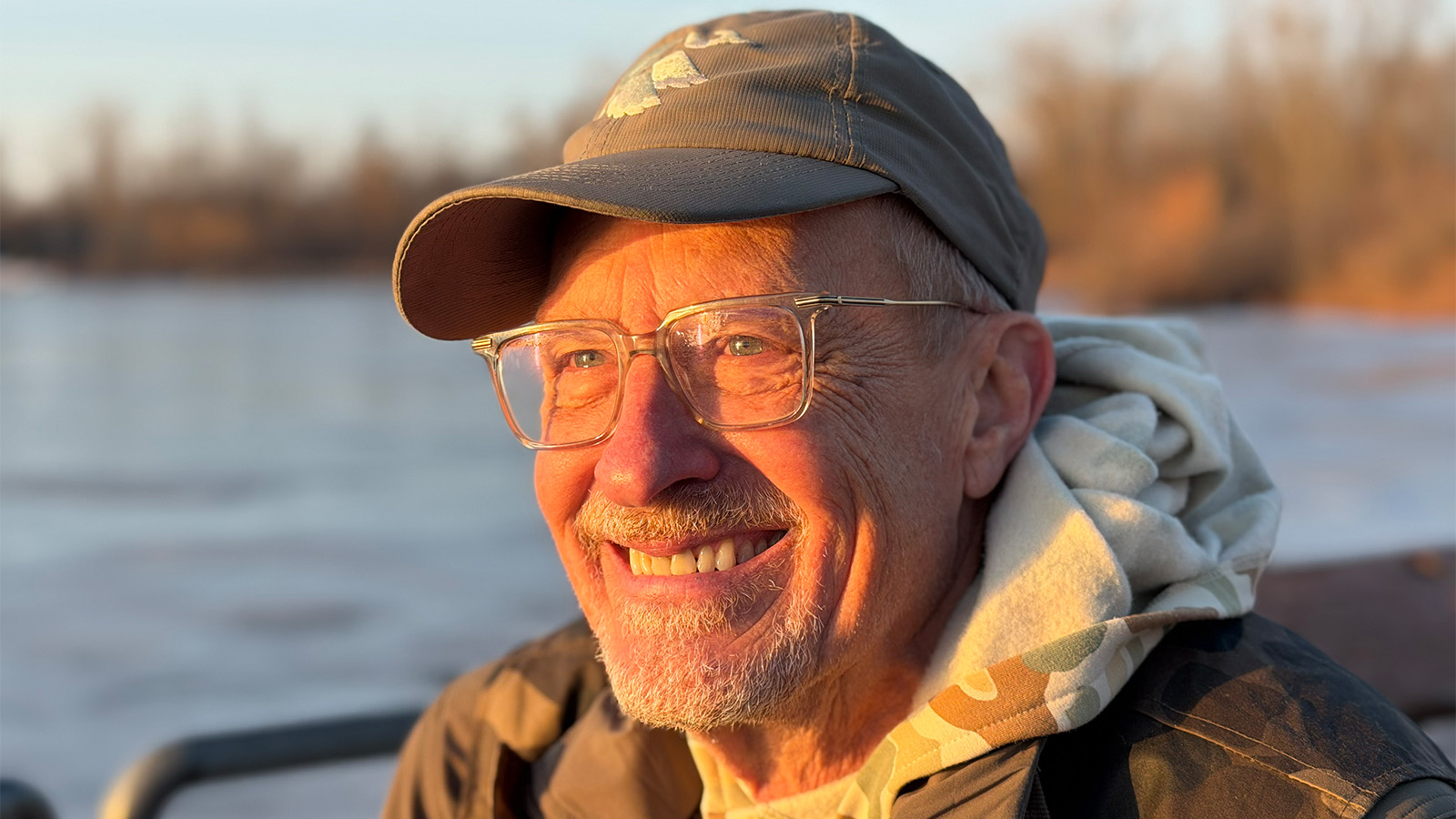 A man wearing a hat and glasses smiling.