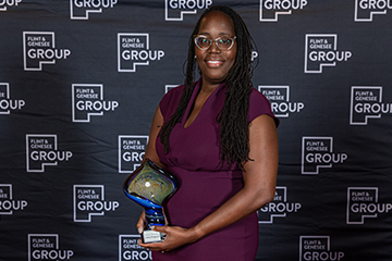 A woman holds a trophy in front of a step and repeat banner that has the Flint & Genesee Group logo.