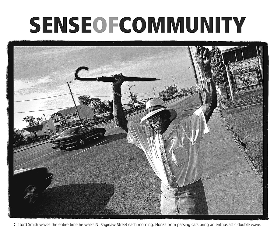 A man holds an umbrella over his head next to a road. A headline reads Sense of Community and a photo caption reads Clifford Smith waves the entire time he walks N. Saginaw Street each morning. Honks from passing cars bring an enthusiastic double wave.