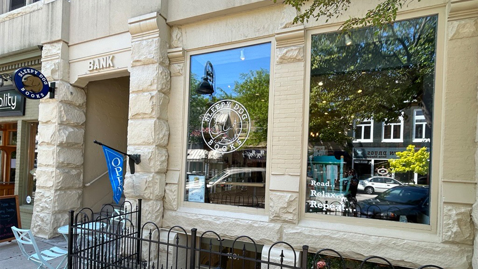 Street view of the front of a tan brick building with two large windows. One window says 