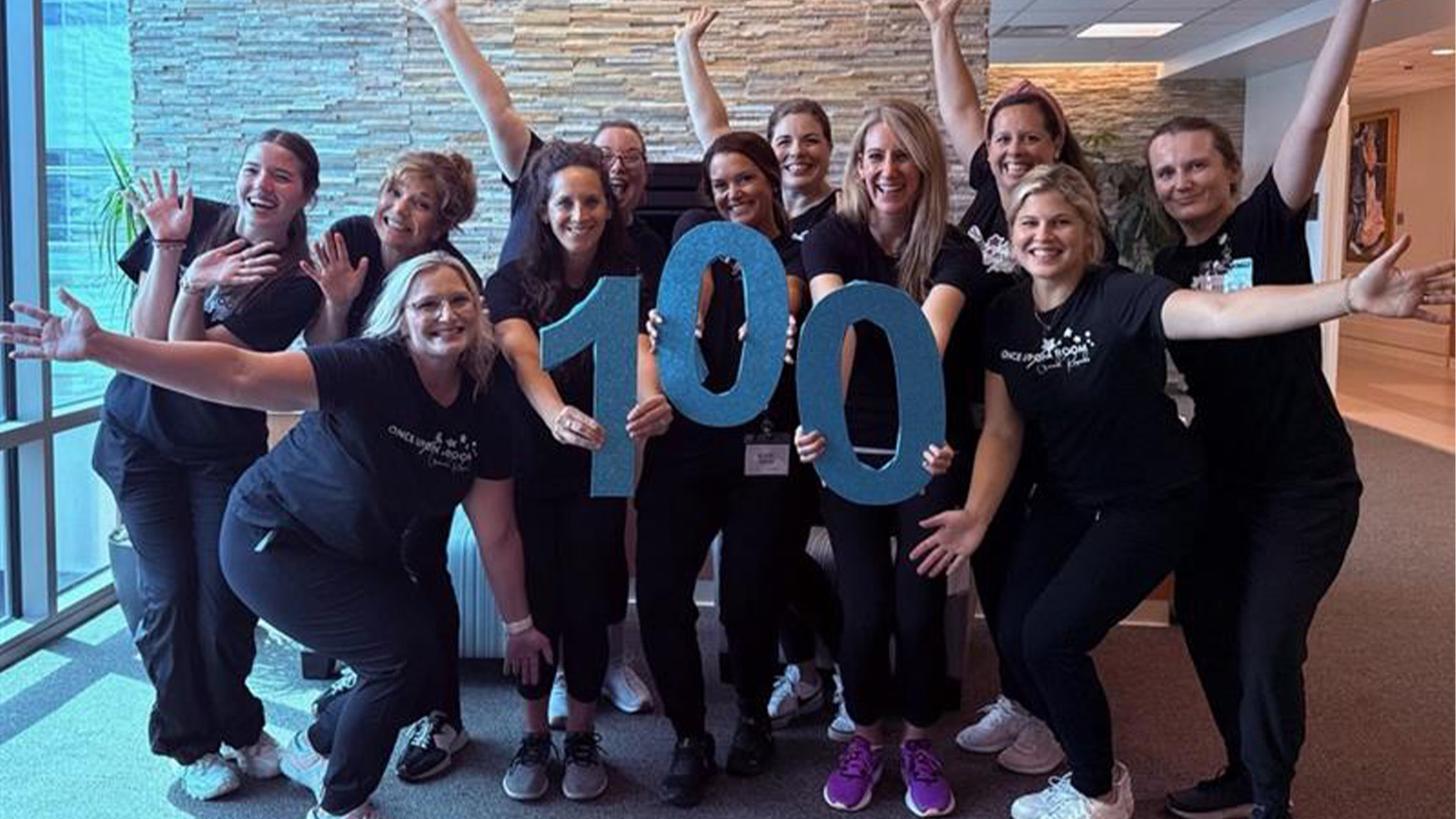 A group of women holding up blue numbers of 1-0-0 to represent the number 100.