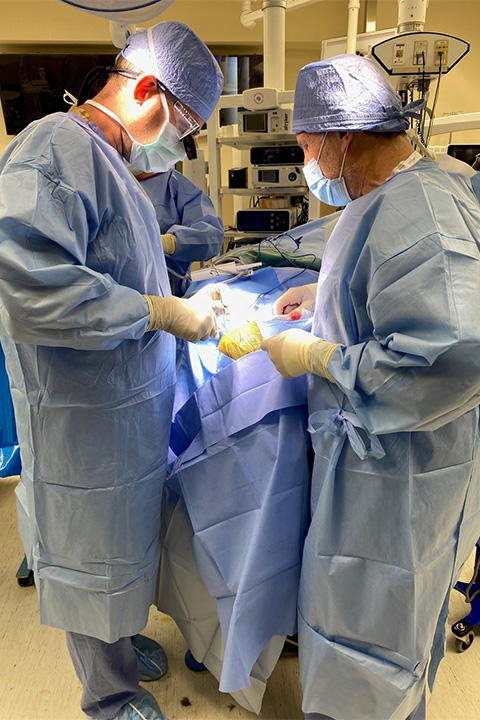 Two men with scrubs on operate inside a hospital room.