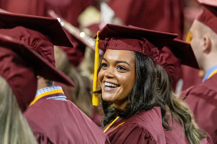 A Central Michigan University graduate is seated, wearing a cap and gown, and smiling.