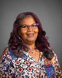 Elizabeth Husbands-200x250 Professional photo of Elizabeth Husbands, Center for Student Inclusion and Diversity-Dedicated Counselor, wearing glasses and a multi-colored blouse against a grey background.