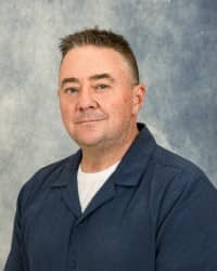 26-08-25 Scott Aldrich-7 Profile picture of Scott Aldrich. He is wearing a blue button down with a white shirt underneath. He has short hair and a blue and gray background.
