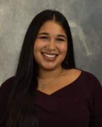 200x250 26-10-01_Maya Vasquez-3 Maya Vasquez, Oros Well-th Scholar and COMPASS Peer Educator. Dark long hair, wearing a dark maroon shirt in front of a grey background.