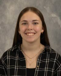 200x250 26-10-01_Olivia Thomson-4 Olivia Thomson, Oros Well-th Scholar and COMPASS Peer Educator. Long dark hair, wearing a black plaid shirt, two necklaces, in front of a grey background.