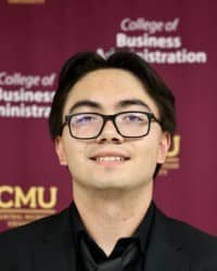 200x250 Jacob Jensen Professional Headshot Jacob Jensen, Oros Well-th Scholar and COMPASS Peer Educator. Dark hair, glasses, wearing a black dress shirt and jacket, in front of the College of Business Administration Background.