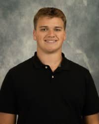 Blake Dennis, Oros Well-th Scholar, COMPASS Peer Educator. Blonde hair, wearing a black polo in front of a grey background.