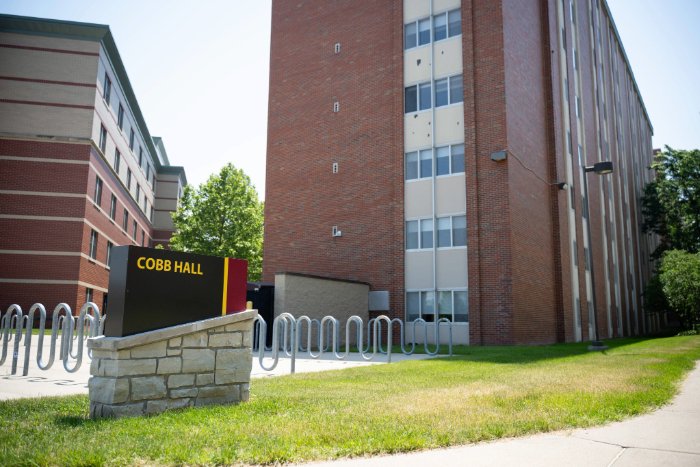 Cobb Hall sign in front of a tall red brick residence hall with vertical windows and bike racks nearby.