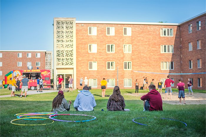 Herrig Activity 01 A group of people sitting on grass in front of Herrig Hall with hula hooping and volleyball occurring in the background.