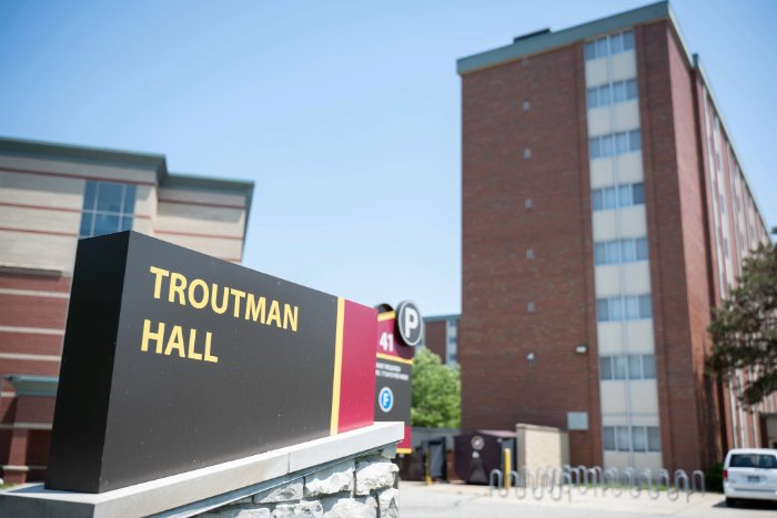 Troutman Hall sign in front of a tall red brick residence building with vertical windows and nearby bike racks.