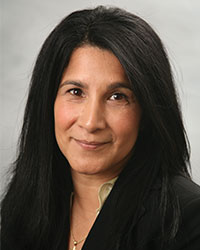 Woman with dark long hair and black blazer smiles for a headshot photo.