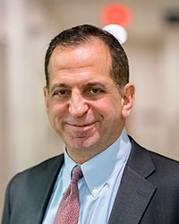 A man smiles for a headshot image with dark hair, and blue dress shirt and gray blazer.