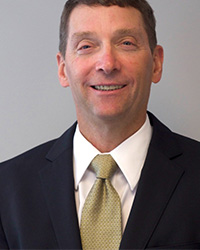 Man smiling wearing black suit jacket, white collared shirt and green tie.