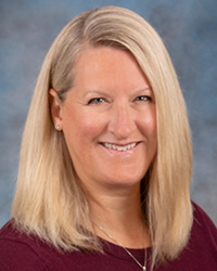 Woman with blonde hair wearing maroon shirt smiling against blue background.