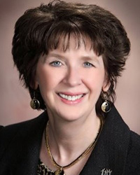 Woman with short brunette hair smiling wearing a black jacket.