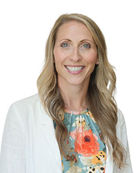 woman with blonde hair smiling with white jacket and colorful shirt against white background.