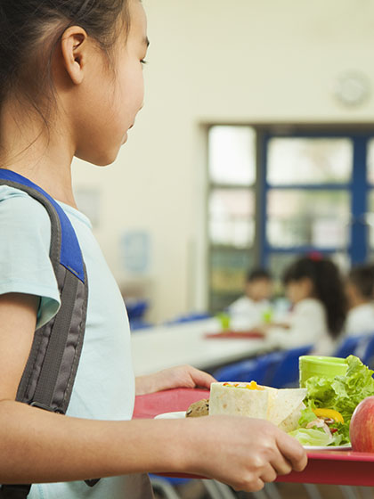 A girl carries a tray of food into a school cafeteria.